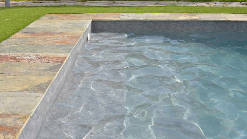 Sfeerbeeld van een buitenzwembad met stenen boord en brede ingewerkte trap, afgewerkt met folie Alkorplan Touch textuur "Prestige"